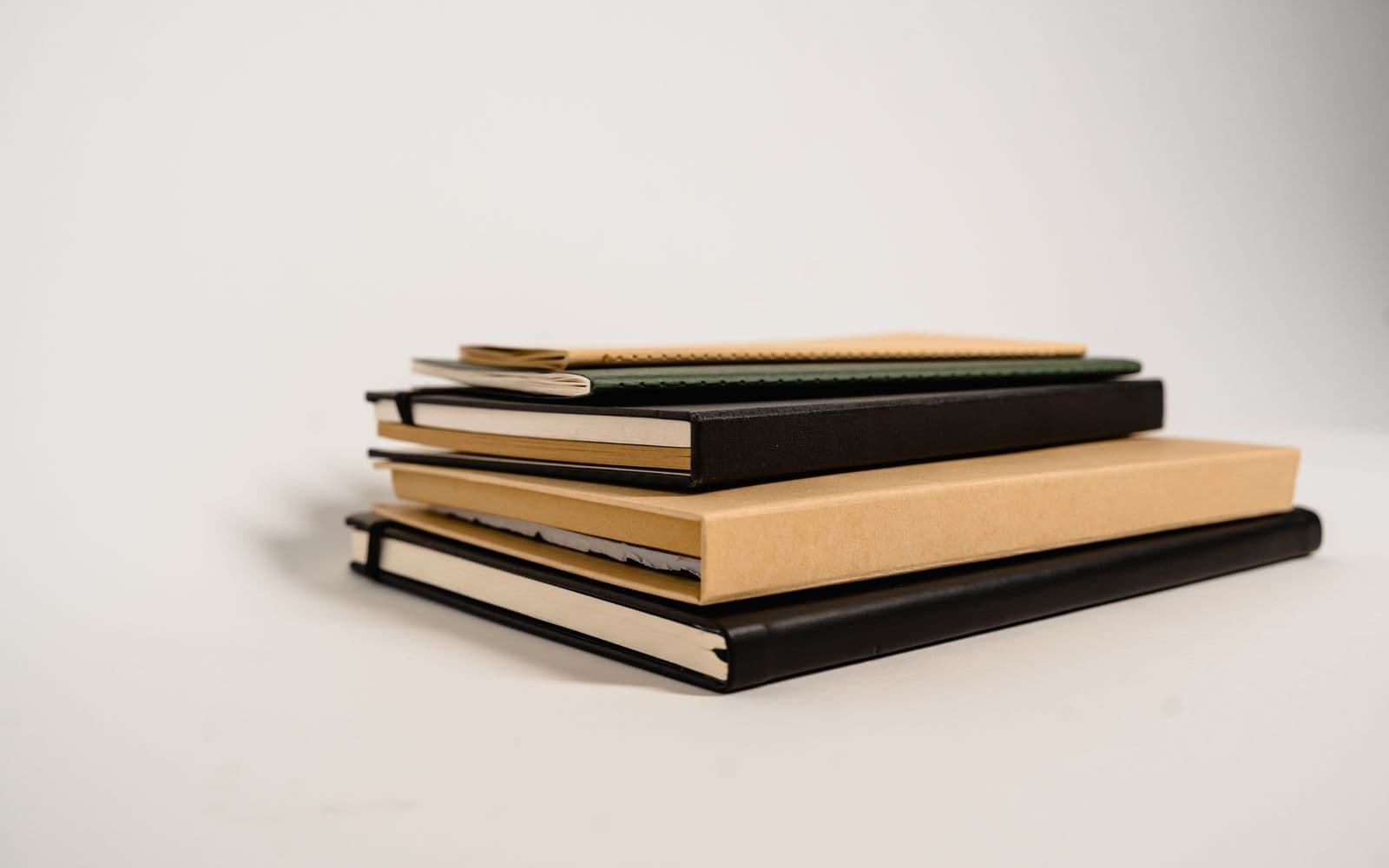 A stack of hardcover journals in black, green and kraft
